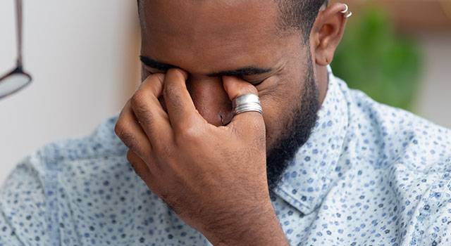 Man with hand on face rubbing eyes, showing signs of fatigue or stress