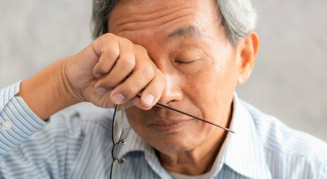 Elderly man rubbing eyes, possibly indicating eye strain or discomfort